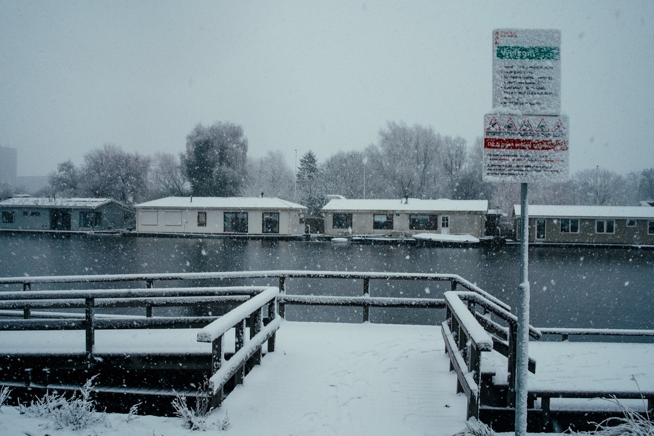 Snow settling on a waterside railing and a moored boat