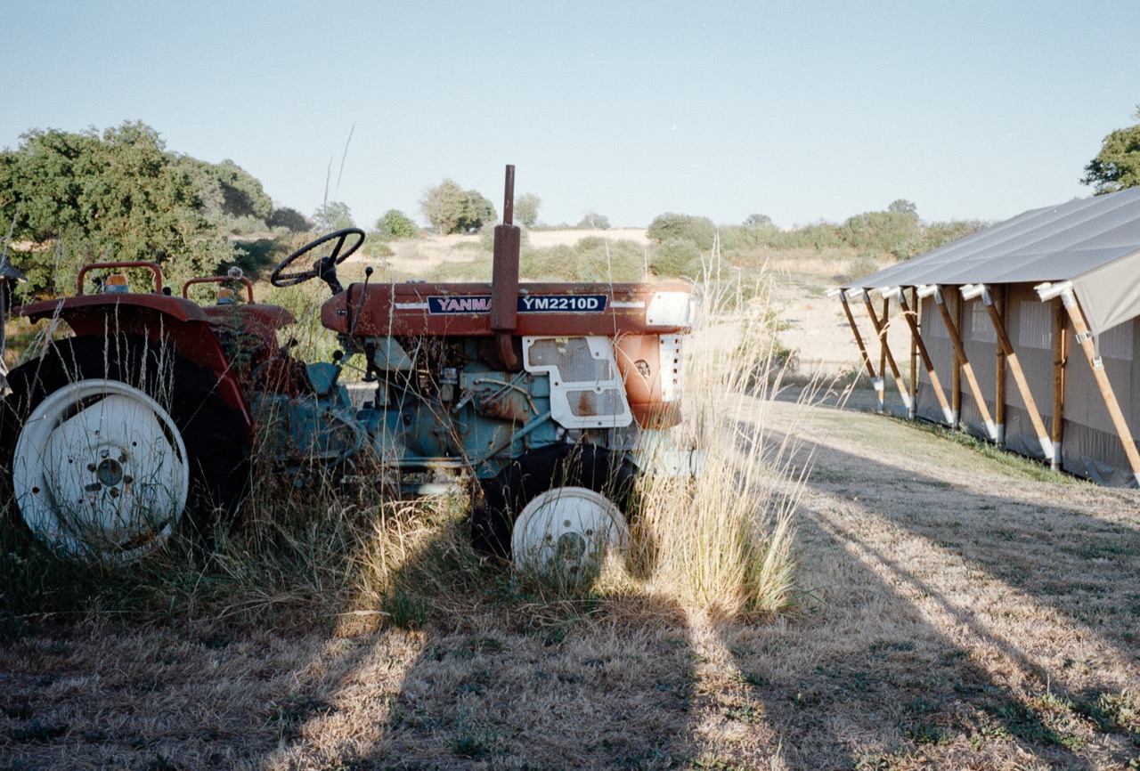 A red tractor beside a greenhouse in a sunlit field
