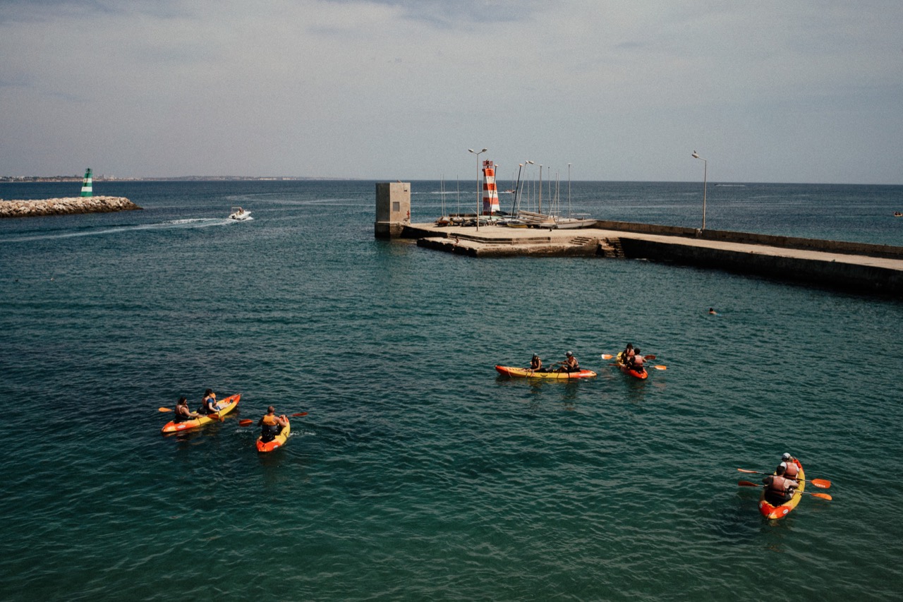 Kayakers crossing blue water beside a harbour breakwater