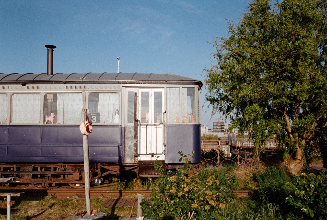 A vintage railway carriage beside trees under a blue Amsterdam sky