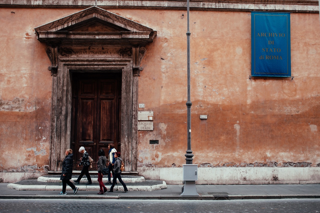 Pedestrians passing an ornate doorway in a warm orange facade