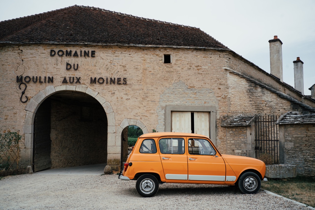 A small orange car parked outside a pale stone building