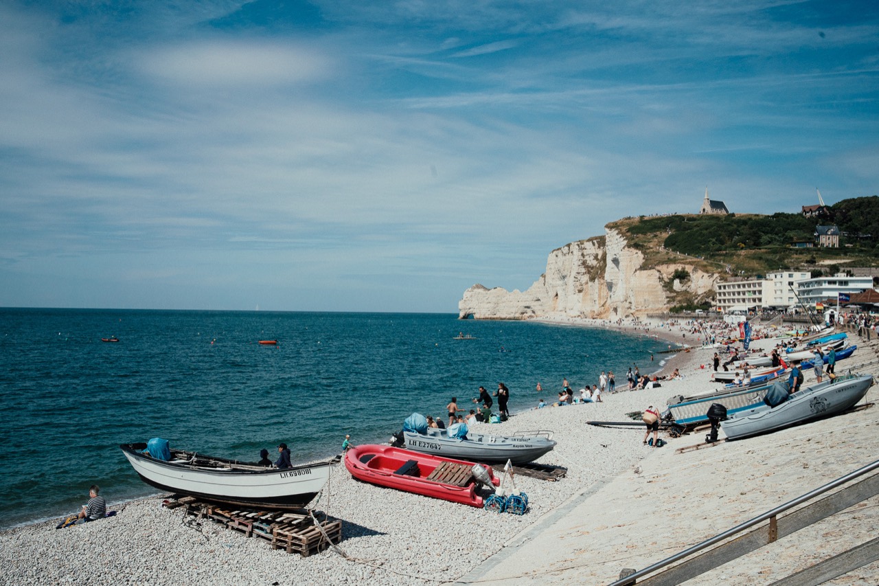 Small boats resting on a pebble beach below white coastal cliffs
