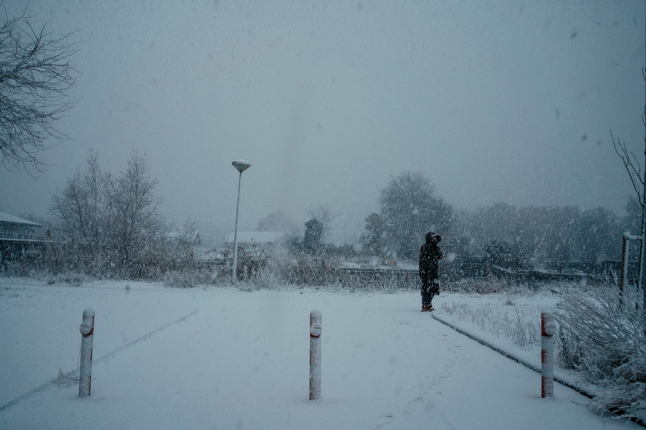 A lone figure crossing a snow-covered landscape in falling snow